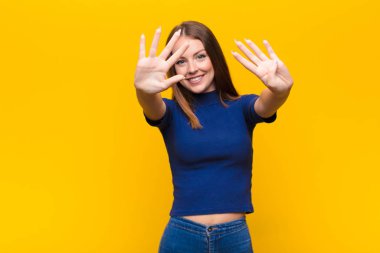 Genç kızıl saçlı kadın gülümsüyor ve arkadaş canlısı görünüyor. Dokuz ya da dokuzuncu numarayı gösteriyor. Eli önde, düz duvara doğru sayıyor.