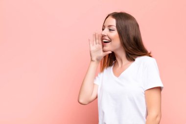 Genç kızıl saçlı kadın profil görüntüsü, mutlu ve heyecanlı görünüyor, bağırıyor ve düz duvara karşı alanı kopyalamak için çağırıyor.