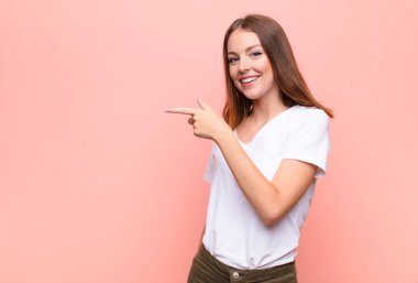 Genç kızıl saçlı kadın heyecanlı ve şaşırmış görünüyor. Yana ve yukarıya doğru düz duvara uzayı gösteriyor.