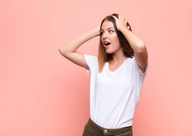 Genç, kızıl saçlı, ağzı açık bir kadın, korkunç ve şok olmuş görünüyor, korkunç bir hata yüzünden, düz duvara karşı ellerini kaldırıyor.