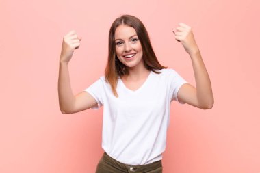 Genç kızıl saçlı kadın inanılmaz bir başarıyı kutluyor. Kazanan gibi. Heyecanlı ve mutlu görünüyor. yassı duvara karşı