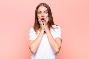 Genç kızıl saçlı kadın şok olmuş ve korkmuş hissediyor. Ağzı açık ve elleri düz duvara yaslanmış.