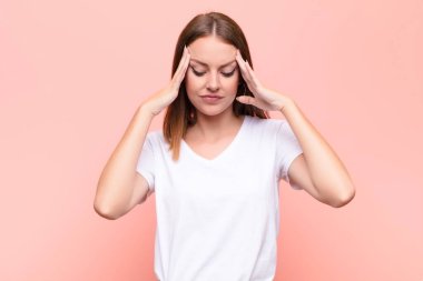 Genç kızıl saçlı kadın stresli ve hayal kırıklığına uğramış görünüyor. Baskı altında çalışıyor. Başı ağrıyor ve düz duvara karşı sorunları var.