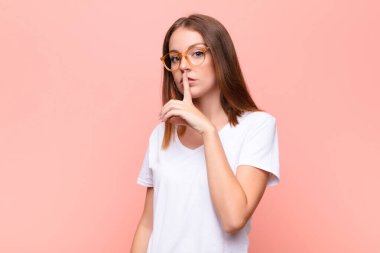 Genç kızıl saçlı kadın sessizlik ve sessizlik istiyor, parmağıyla ağzının önünde işaret ediyor, 