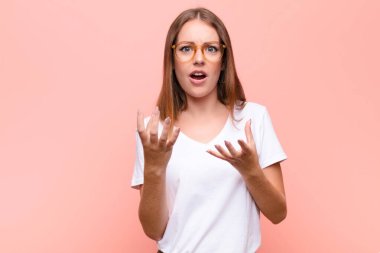 Genç kızıl saçlı kadın umutsuz ve sinirli görünüyor, stresli, mutsuz ve sinirli, bağırıyor ve düz duvara karşı bağırıyor.