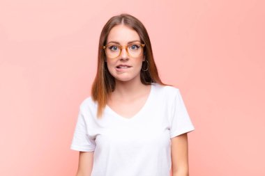 Genç kızıl saçlı kadın şaşkın ve şaşkın görünüyor, gergin bir hareketle dudağını ısırıyor, düz duvara karşı sorunun cevabını bilmiyor.