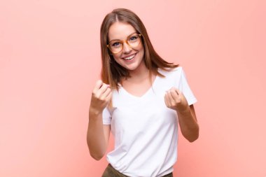 Genç kızıl saçlı kadın zaferle bağırıyor, gülüyor, mutlu ve heyecanlı hissederken düz duvara karşı başarıyı kutluyor.