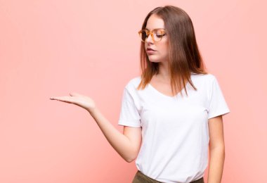 Genç kızıl saçlı kadın kendini mutlu hissediyor ve gülümsüyor. Bir objeye ya da duvara yaslanmış bir konsepte bakıyor.