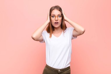 Genç kızıl saçlı kadın mutsuz, korkmuş ya da endişeli görünüyor, ağzı sonuna kadar açık ve iki kulağı da düz duvara dayalı.