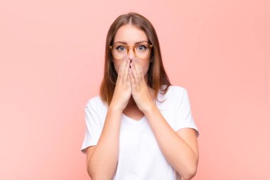 Genç kızıl saçlı kadın endişeli, üzgün ve korkmuş hissediyor, elleriyle ağzını kapatıyor, endişeli görünüyor ve düz duvara karşı işleri berbat ediyor.