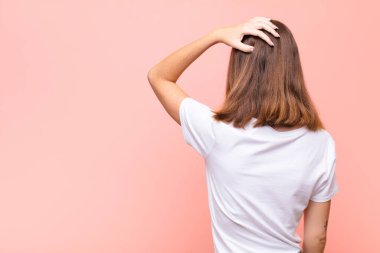 Genç kızıl saçlı kadın bilgisiz ve kafası karışık, bir çözüm düşünüyor, eli kalçasında, diğeri kafasında, düz duvara karşı dikiz manzaralı