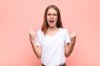 Genç kızıl saçlı kadın sinirli bir ifadeyle bağırıyor ya da yumruklarıyla düz duvara karşı başarıyı kutluyor.