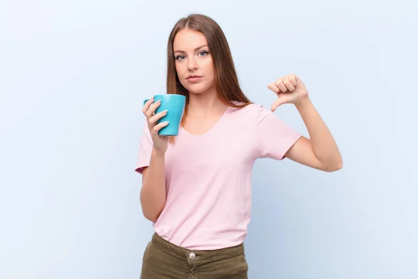 一个红头发的年轻女子 拿着咖啡杯靠着平墙站着 — 图库照片