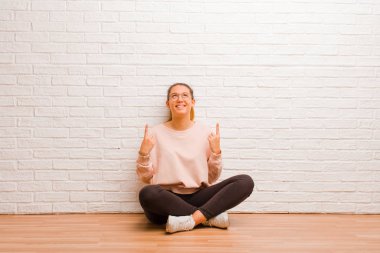 Genç ve güzel bir kadın, tuğla duvarın arkasında, yerde oturuyor.