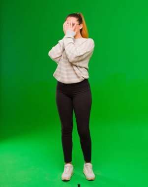 Genç, güzel, Latin bir kadın korkmuş ya da utanmış hissediyor. Gözleri yarı kapalı, elleri yeşil duvarda dikizliyor ya da dikizliyor.