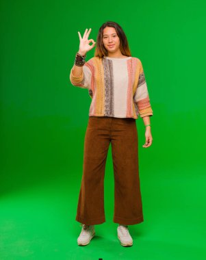 Genç, güzel Latin bir kadın mutlu, rahat ve tatmin olmuş hissediyor. Onayını iyi bir hareketle gösteriyor. Yeşil duvara gülümsüyor.