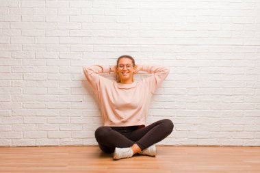 Genç ve güzel bir kadın, tuğla duvarın arkasında, yerde oturuyor.