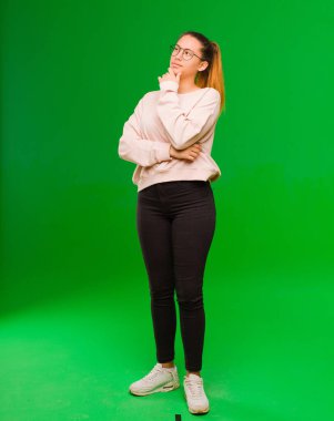 Genç, güzel, Latin bir kadın düşünceli, meraklı ya da hayal kuruyor, hayal kuruyor ve yeşil duvara karşı mekanı kopyalamak istiyor.