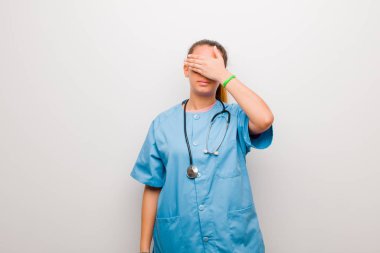 Genç Latin hemşire tek eliyle gözlerini kapatıyor. Korkmuş ya da endişeli hissediyor, merak ediyor ya da körü körüne beyaz duvara karşı bir sürpriz bekliyor.