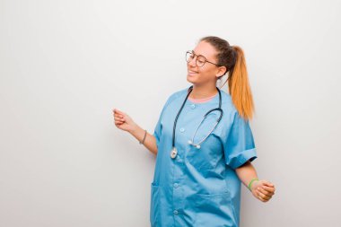 Genç Latin hemşire gülümsüyor, kaygısız, rahat ve mutlu hissediyor, dans ediyor ve müzik dinliyor, beyaz duvarın karşısındaki bir partide eğleniyor.