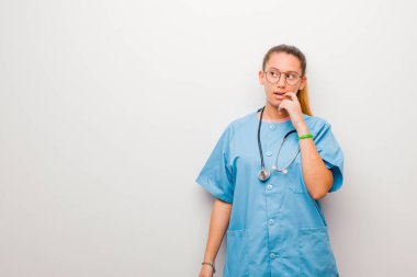 Şaşırmış, gergin, endişeli ya da korkmuş bakışları olan genç Latin hemşire beyaz duvara karşı fotokopi odasına doğru bakıyor.