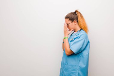 Genç Latin hemşire üzgün, hayal kırıklığına uğramış bir bakışla gözlerini kapatıyor. Ağlıyor, beyaz duvara bakıyor.