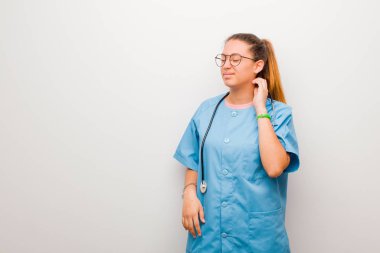 Genç Latin hemşire stresli, hayal kırıklığına uğramış ve yorgun hissediyor. Beyaz duvara karşı endişeli ve sorunlu bir bakışla boynunu ovalıyor.