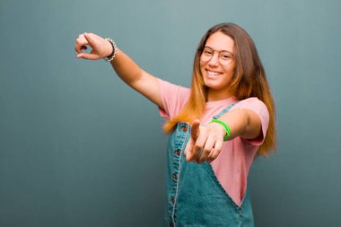 Genç ve güzel Latin kadın mutlu ve kendinden emin, kamerayı iki eliyle gösteriyor ve gülüyor, grunge duvarına karşı seni seçiyor.