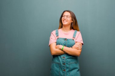 Genç, güzel, Latin bir kadın mutlu, gururlu ve umutlu, merak eden ya da düşünen, kolları çapraz bir şekilde grunge duvarına yaslanmış, fotokopi çekmek isteyen