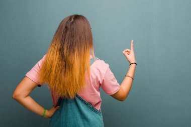 Fotokopi alanında duran ve objeye işaret eden genç, güzel Latin kadın, grunge duvarına karşı dikiz aynası.