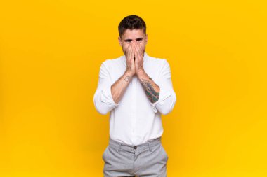 Genç adam mutlu, neşeli, şanslı ve şaşırmış görünüyor. İki elini de düz duvara dayayıp ağzını kapatıyor.