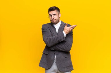 Genç adam kafası karışık ve cahil hissediyor, şüpheli bir açıklamayı merak ediyor ya da düz renkli bir duvara karşı düşünüyor.