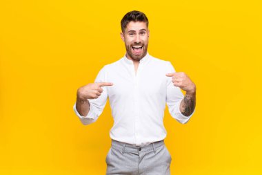 Genç adam kendini mutlu, şaşırmış ve gururlu hissediyor. Heyecanlı ve şaşkın bir bakışla düz renkli duvara bakıyor.