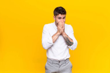 Genç handosme adam endişeli, umutlu ve dindar hissediyor, sadık bir şekilde avuç içleriyle dua ediyor, düz renkli duvara karşı af diliyor.