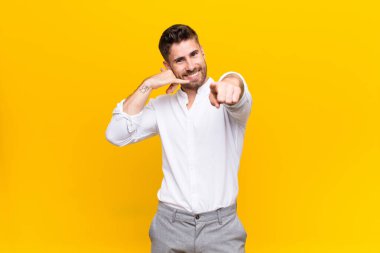 Genç Handome neşeyle gülümseyen ve kamerayı işaret eden adam daha sonra bir arama yaparken düz renkli duvara karşı telefonla konuşuyor.