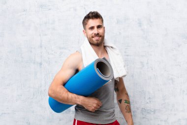 Genç adam yoga minderli düz renkli duvara karşı. spor konsepti