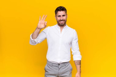 Genç adam kendini mutlu, rahat ve tatmin olmuş hissediyor. Onayını iyi bir hareketle gösteriyor. Renk duvarına gülümsüyor.