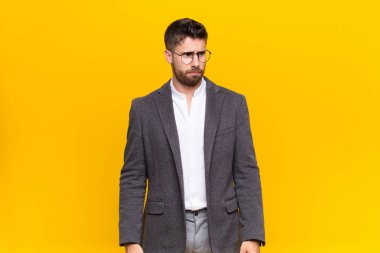 Genç adam üzgün, üzgün ya da kızgın hissediyor ve olumsuz bir tavır takınıyor, düz renk duvarına karşı anlaşmazlık içinde.