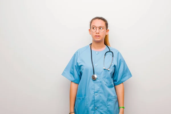 young latin nurse looking worried, stressed, anxious and scared, panicking and clenching teeth against white wall