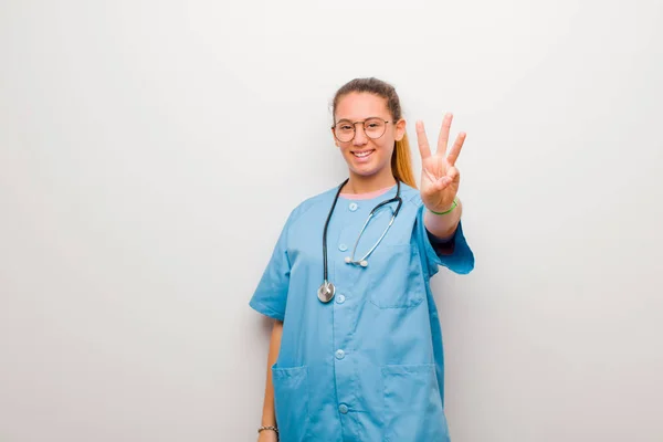 若いラテン語の看護師は笑顔で友好的に見え 前方に手で3番目または3番目を示し 白い壁に対してカウントダウンします — ストック写真