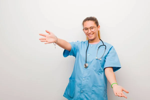 young latin nurse smiling cheerfully giving a warm, friendly, loving welcome hug, feeling happy and adorable against white wall