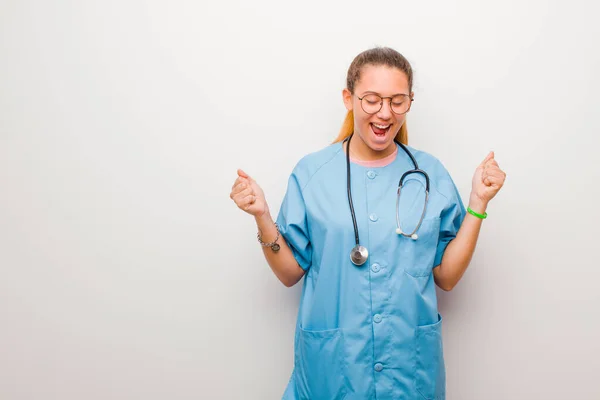 young latin nurse looking extremely happy and surprised, celebrating success, shouting and jumping against white wall