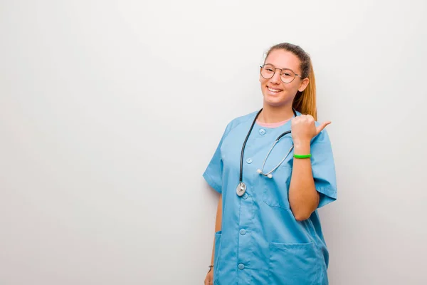 若いラテン語の看護師は喜んで笑顔で幸せそうに見えます白壁に対して両方の親指で気楽で肯定的な感じ — ストック写真
