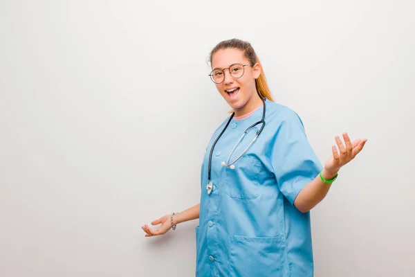 young latin nurse looking happy, arrogant, proud and self satisfied, feeling like a number one against white wall