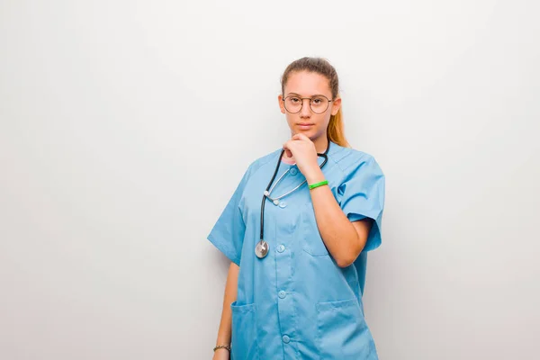 若いラテン語の看護師は深刻で混乱し不確定で思慮深く白い壁に対する選択肢や選択肢の中で — ストック写真