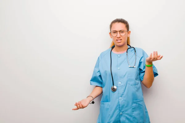 young latin nurse feeling clueless and confused, not sure which choice or option to pick, wondering against white wall