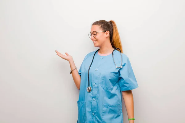 ラテン語の若い看護師は幸せと笑顔を気軽に感じながら白い壁に向かって手に持っている物や概念を探し — ストック写真