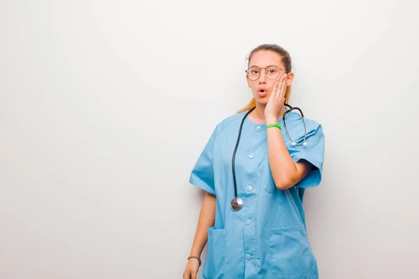 若いラテン語の看護師はショックを受け 白い壁に対して口を開けて不信に手をつないで顔を持って驚いた — ストック写真