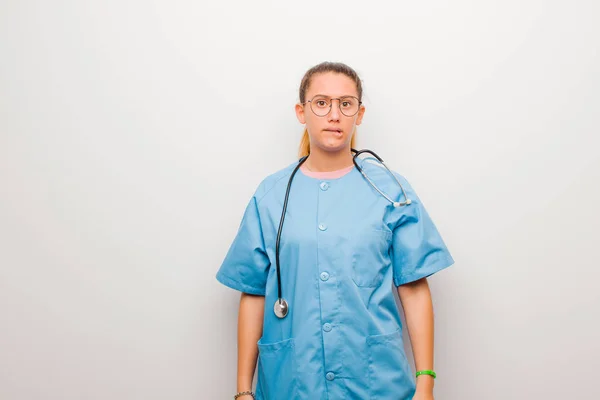 young latin nurse feeling clueless, confused and uncertain about which option to pick, trying to solve the problem against white wall