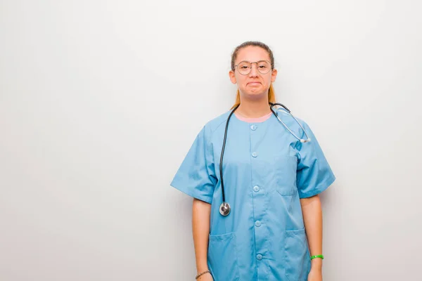 young latin nurse feeling sad and stressed, upset because of a bad surprise, with a negative, anxious look against white wall